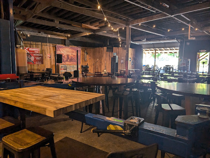 The main garage at Cofer's Garage: wooden tables, bar stools, string lights, and the stage at the back