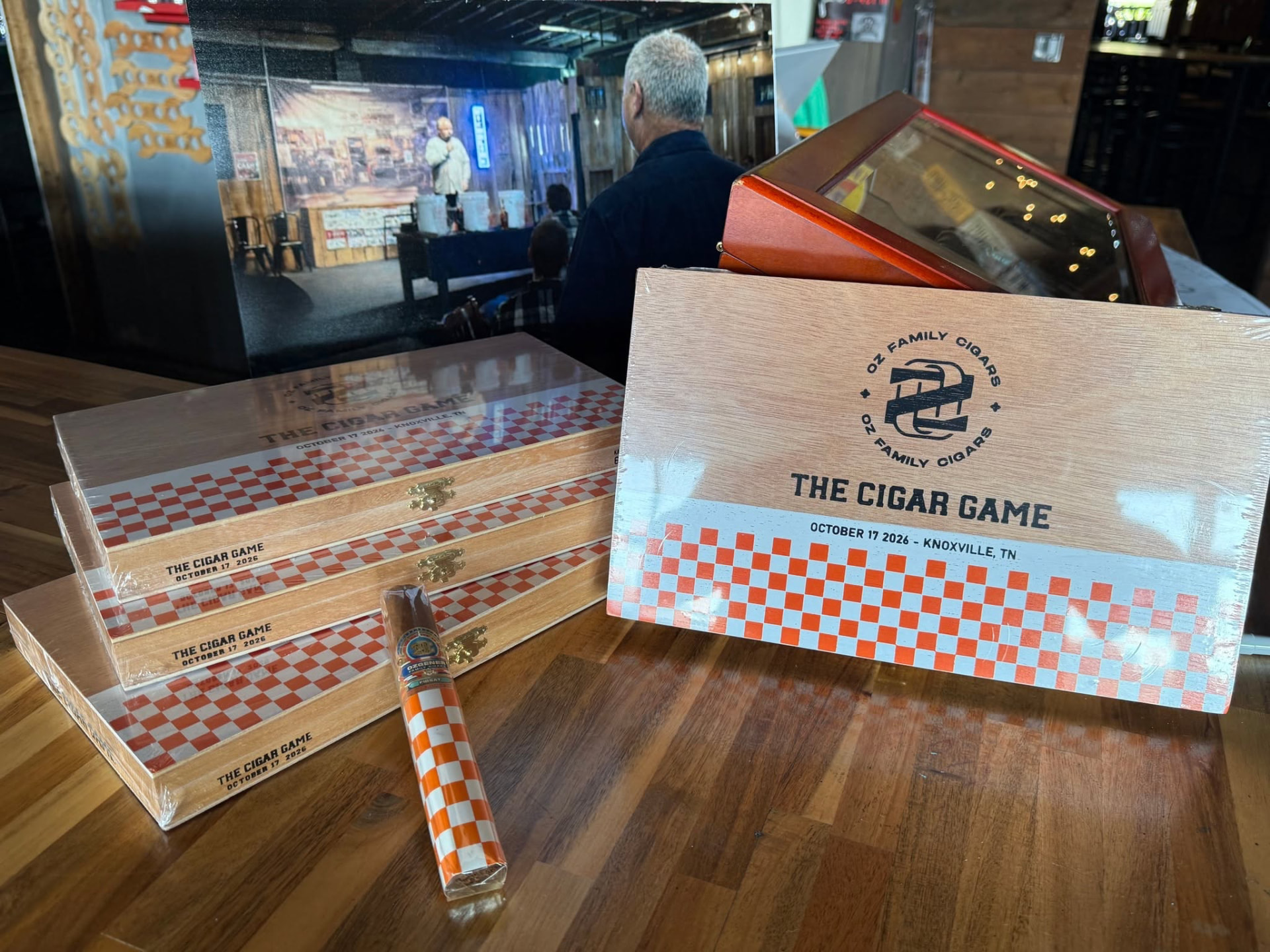 Cigar boxes on a wooden table inside Cofer's Garage during an event, with the stage visible behind